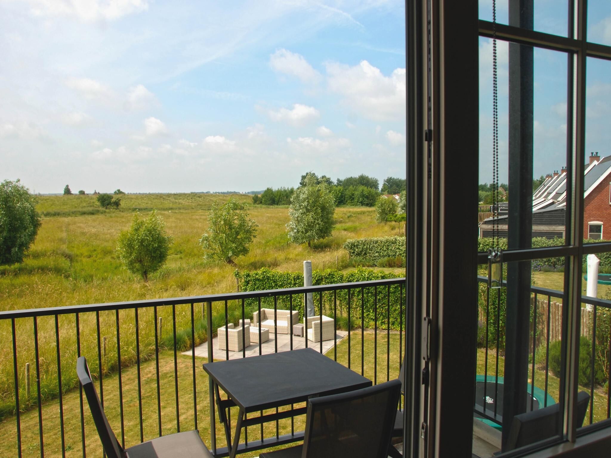 Varanda com mesa e cadeiras, com vista para um campo gramado e área residencial.