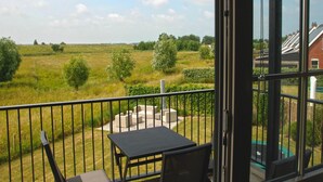 En balkon med et bord og stole, udsigt over en græsplæne og et boligområde.