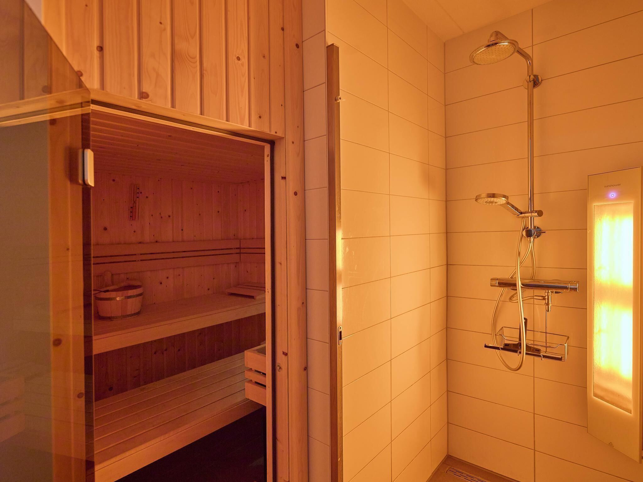 Un sauna avec des bancs en bois et une porte en verre, un espace douche avec une paroi en verre et un mur carrelé.