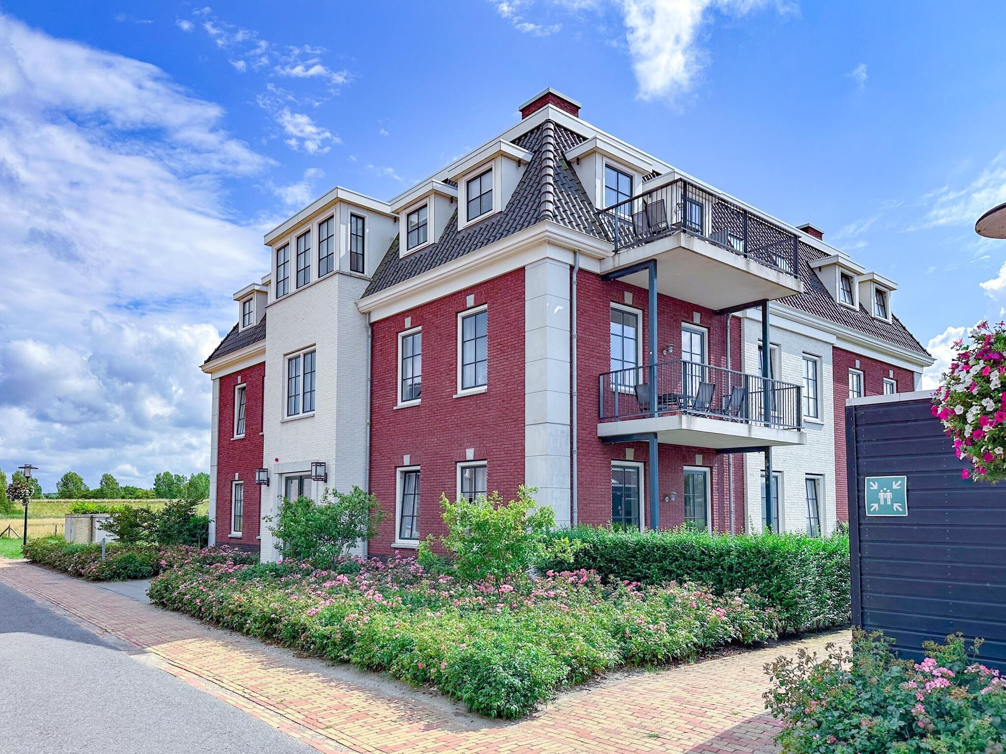 Een woonhuis met twee verdiepingen, voorzien van een balkon, omgeven door verzorgde tuinen en een verharde oprit.