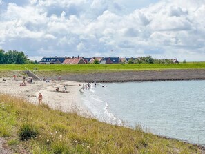 Uma praia com pessoas aproveitando a água, uma área gramada e casas ao fundo.