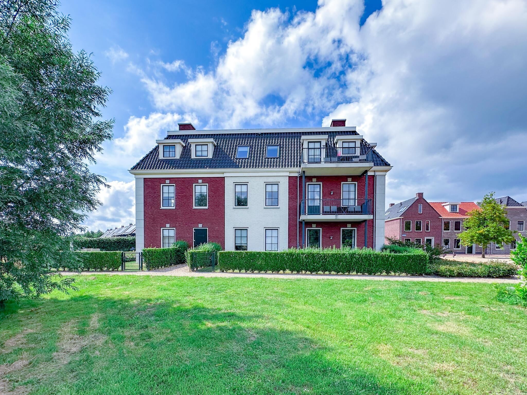 Ein zweistöckiges Wohngebäude mit roter und weißer Fassade, zahlreichen Fenstern und einem Balkon.