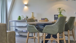 Zona de menjador moderna amb taula de fusta, cadires amb fons verds i un ramader decoratiu.