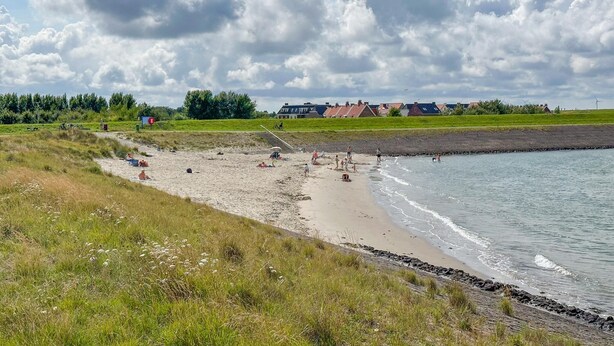 Ein Strand mit Menschen, einer Rasenfläche und Häusern im Hintergrund.