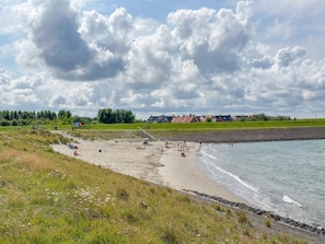 Ein Strand mit Menschen, einer Rasenfläche und Häusern im Hintergrund.