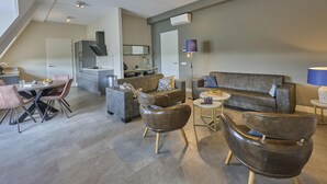 Ein modernes Wohnzimmer mit einer Couch, Sesseln, einem Esstisch und einer Küchenzeile.