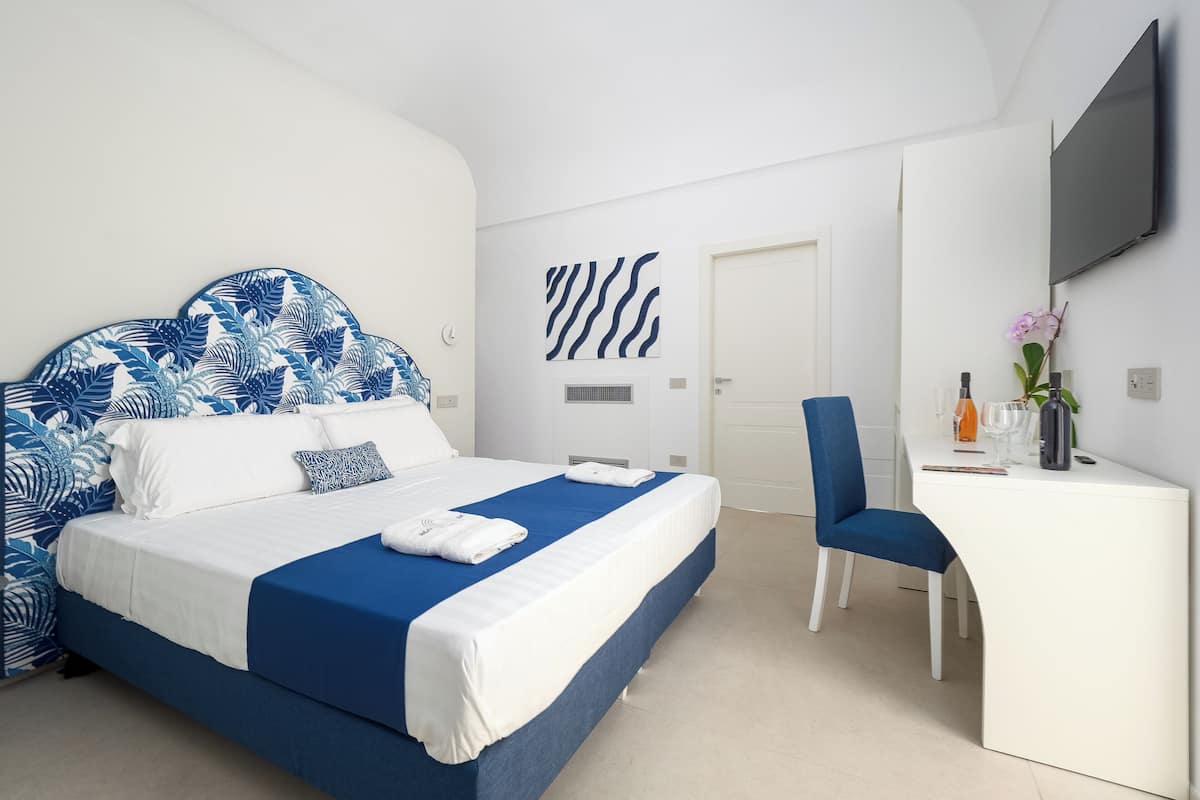 A modern hotel room with a large bed, a desk, and a TV.