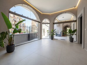 A spacious corridor with arched ceilings and large windows, potted plants, and a view of the outside buildings. - Blue Sky Luxury Palace (Meta)