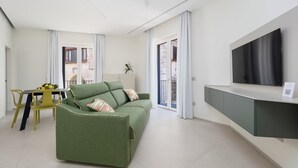 Una sala de estar moderna con un sofá verde, una mesa de comedor con sillas amarillas, un televisor de pantalla plana en la pared y un balcón con puertas correderas.