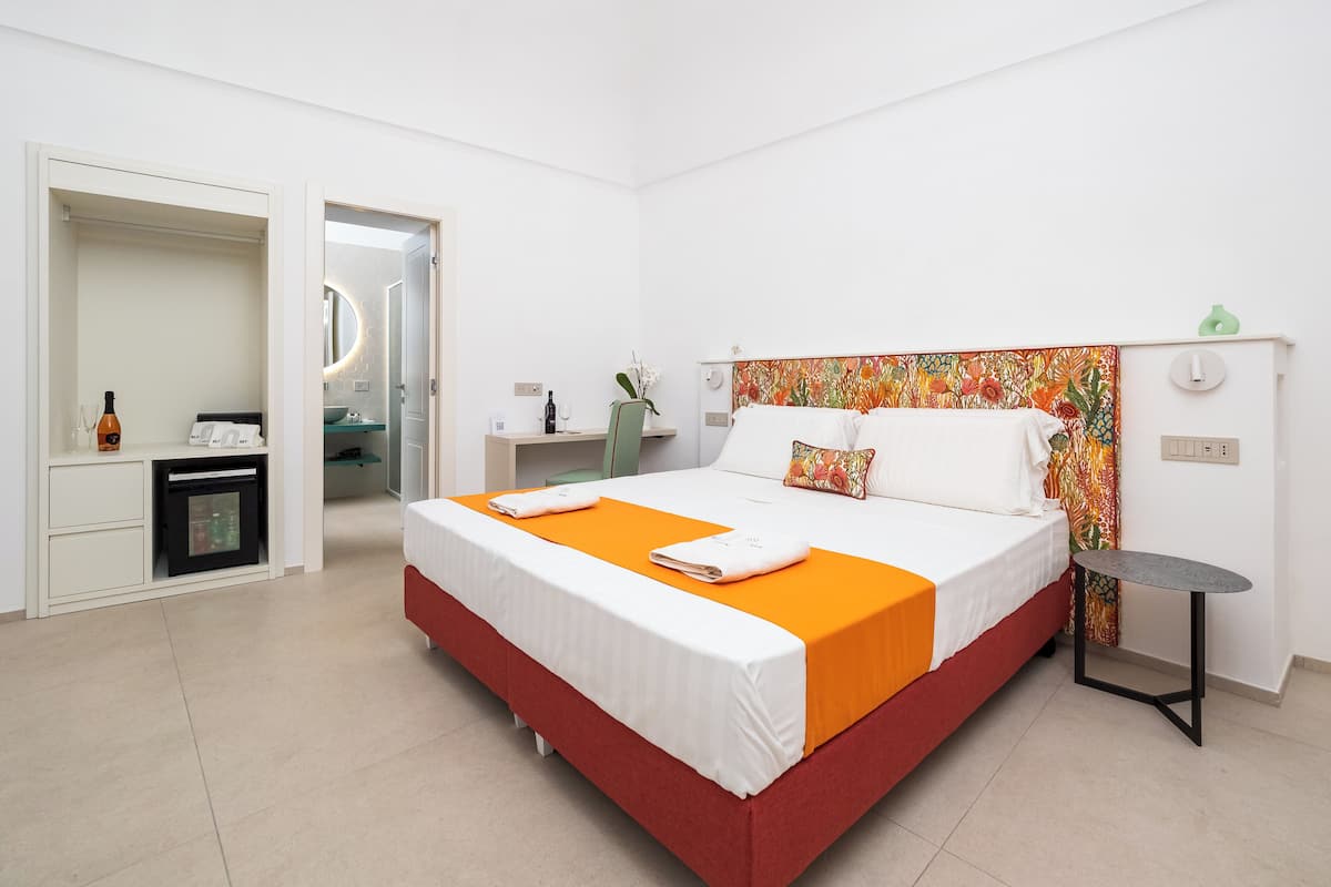 A hotel room with a bed, a desk, a chair, a small table, and a mirror.