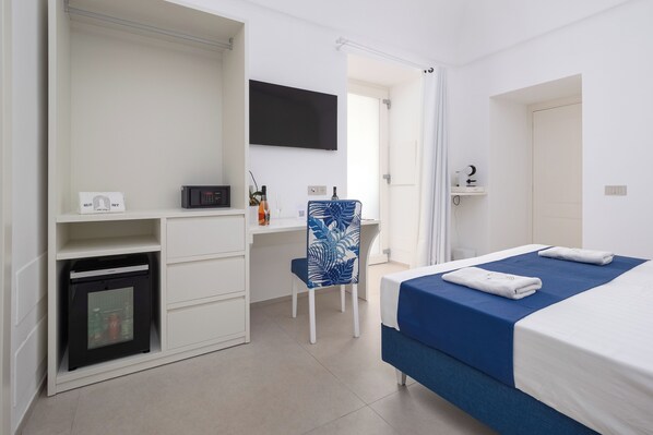 Un dormitorio con cama, escritorio, silla, televisor y minibar.