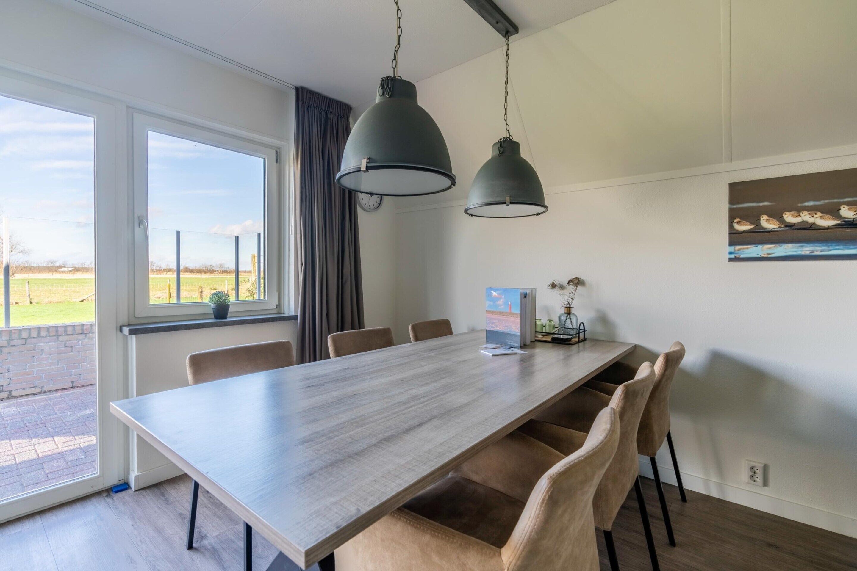 A modern dining area with a long table, six chairs, and two hanging pendant lights.