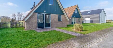 Une maison moderne à deux étages, avec une façade en briques, de grandes portes-fenêtres coulissantes et un petit jardin à l’avant.