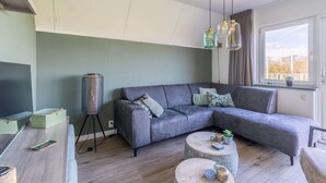 A modern living room with a grey sectional sofa, a round coffee table, and a floor lamp. - Tastefully and Modernly Furnished Holiday Home for 6 Persons (De Waal)