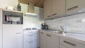 A modern kitchen with white cabinets, a stainless steel sink, and a built-in oven. - Tastefully and Modernly Furnished Holiday Home for 6 Persons (De Waal)