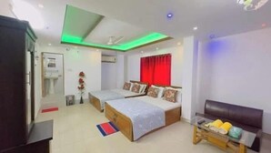 Habitación de hotel con dos camas, un escritorio, una silla, una mesita, un cesto de basura y una ventana con cortinas rojas.