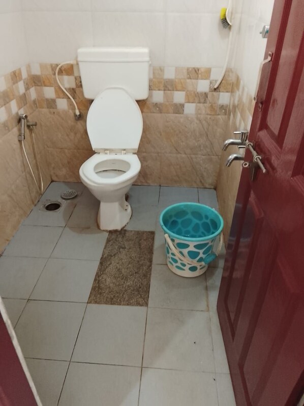 A small bathroom with a toilet, a shower, and a bucket. - SOHAN BOARDING AND LODGING (Udupi)