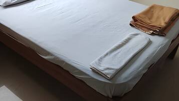 Una cama individual con ropa blanca, una toalla doblada y una colcha al lado derecho.