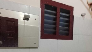 A bathroom with a white sink, a mirror, a red-framed window, and a shower. - SOHAN BOARDING AND LODGING (Udupi)