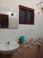A bathroom with a white sink, a mirror, a red-framed window, and a shower.