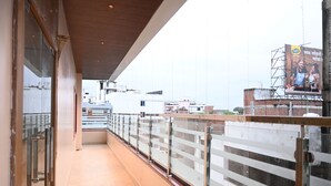 A corridor with a glass railing, leading to a balcony with a view of buildings. - Hotel KIR International (Awleshpur)