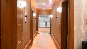 A hotel hallway with wooden paneling, marble flooring, and wall-mounted light fixtures. - Hotel KIR International (Awleshpur)