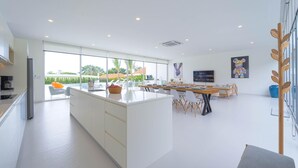 Une cuisine moderne dotée d’un grand îlot central, d’un coin repas avec une table en bois et d’une vue sur l’extérieur.