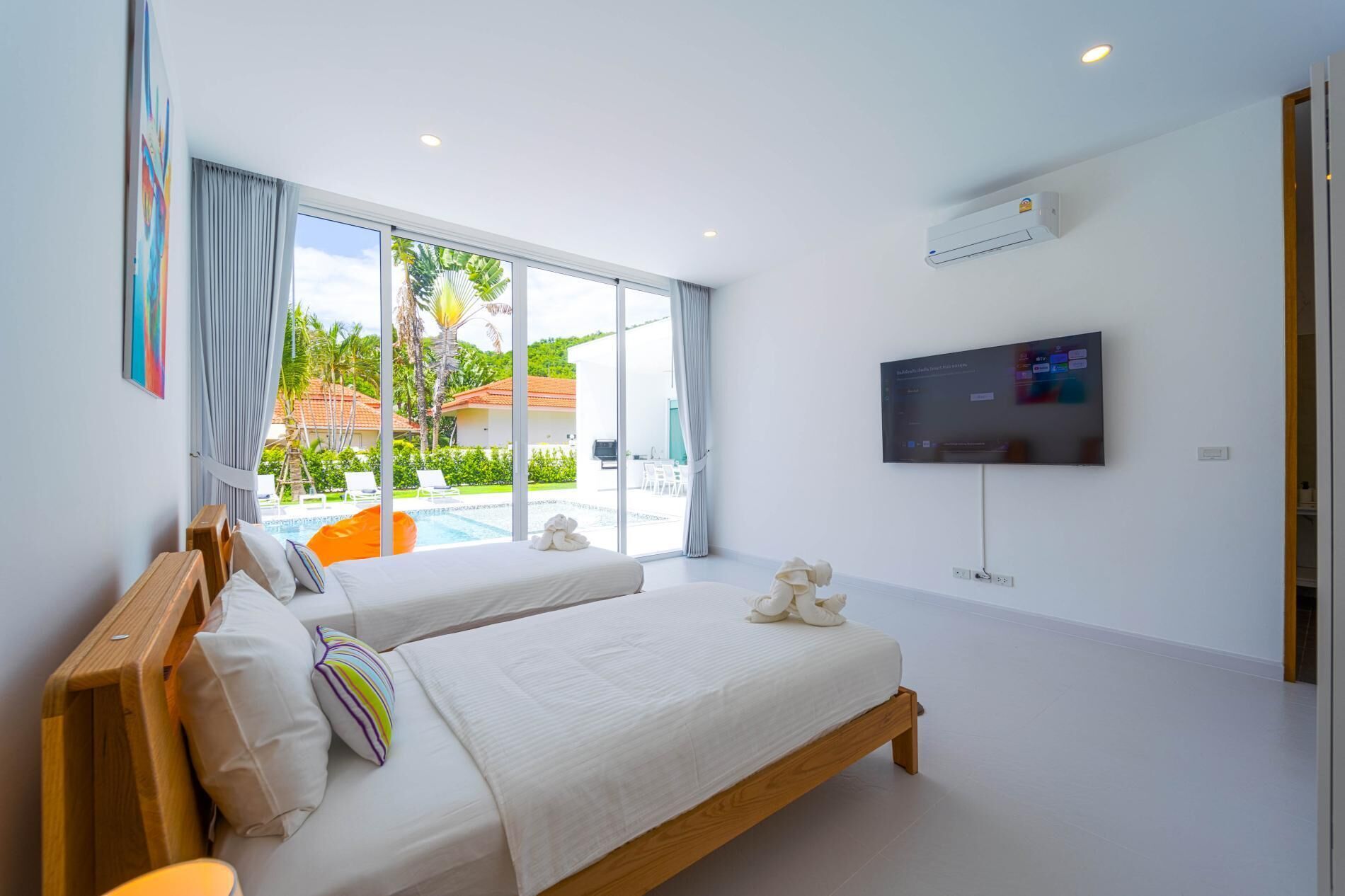 A modern hotel room with a large bed, a TV, and a view of a pool and greenery.