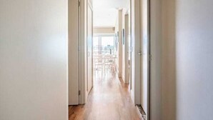 A hallway with wooden flooring and white walls, leading to a balcony with a view of the city. - Waterfront Nest Above Viaduct Harbour Free Parking (Auckland)