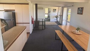 Une cuisine moderne dotée d’un réfrigérateur encastré, un coin repas avec un banc en bois et un couloir menant à une autre pièce.