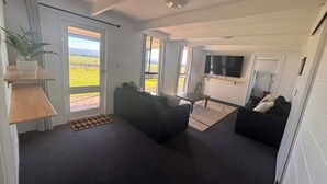 Un salon doté d’un grand téléviseur, d’un canapé, d’une table basse et offrant une vue sur un champ verdoyant par les fenêtres.