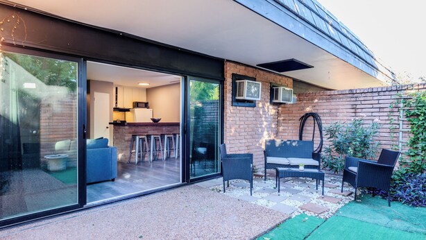 Une maison moderne dotée d’une porte vitrée donnant sur un patio aménagé avec du mobilier d’extérieur et un mur en briques.