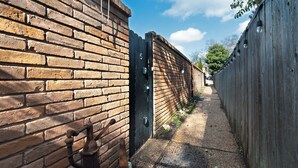 Une ruelle étroite, bordée d’un côté par un mur de briques et de l’autre par une clôture en bois.