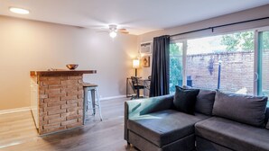 Un salon avec un mur d’accent en briques, un canapé d’angle, un ventilateur de plafond et une grande fenêtre avec des rideaux.