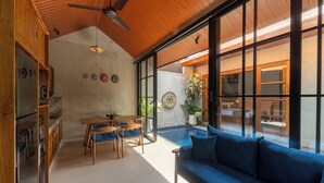 Ein modernes Wohnzimmer mit einem blauen Sofa, Holzboden und großen Fenstern mit Blick auf einen Poolbereich.