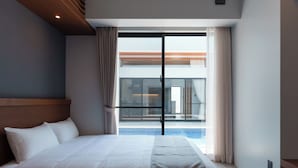 Habitación de hotel con una cama grande, cabecera de madera, vista a una piscina a través de una puerta de cristal y un balcón.