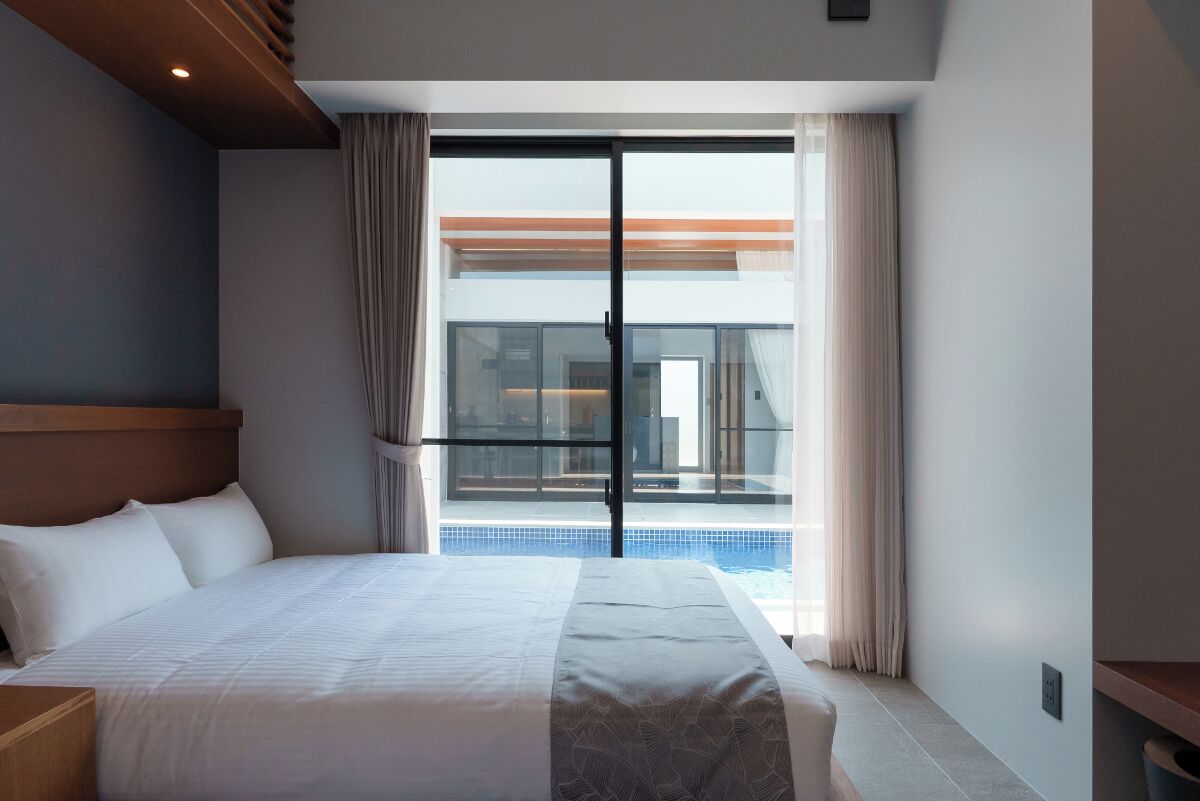Habitación de hotel con una cama grande, vista a una piscina y puerta corredera de vidrio que da a un balcón.