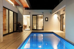A modern indoor swimming pool with clear blue tiles, surrounded by a minimalist architectural design with glass doors and a small seating area. - Bel Tempo Pool Villa (Ishigaki)