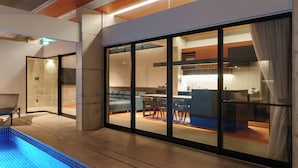 Un interior moderno con piscina, zona de comedor y cocina visibles a través de amplios ventanales.