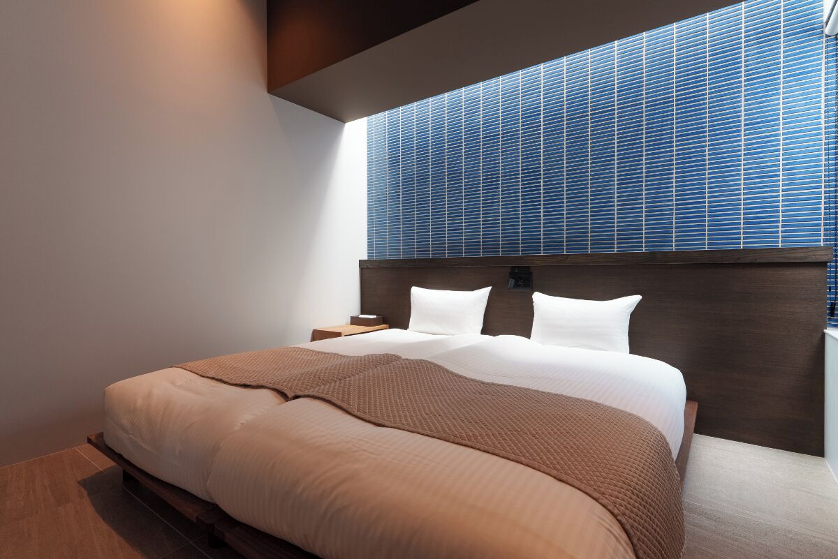 Un dormitorio moderno con una cama grande, cabecera de madera y vistas al cielo a través de una ventana con persianas azules.