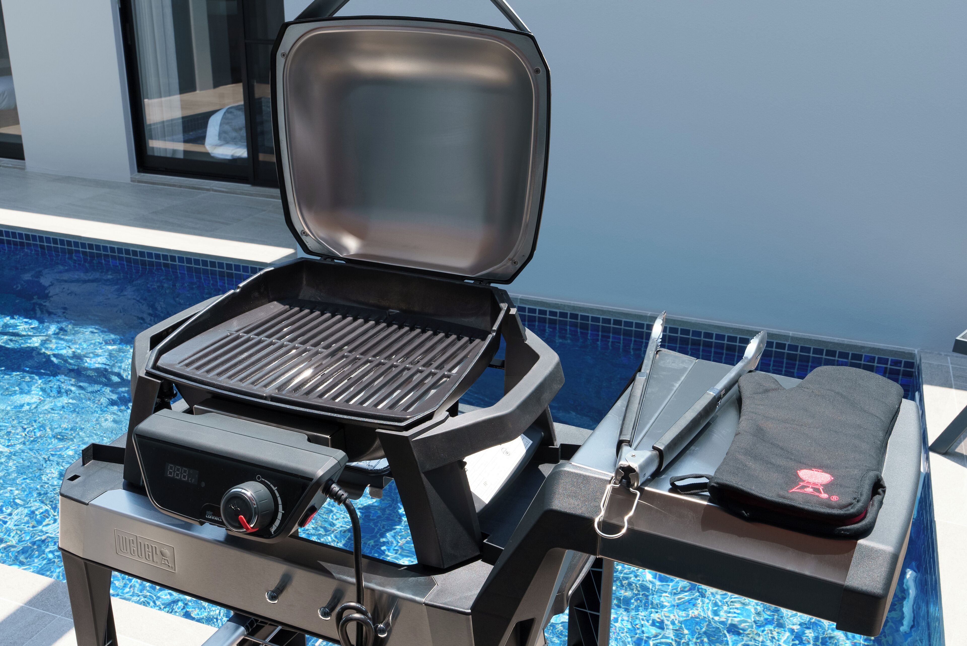 A portable grill with a digital display, positioned near a swimming pool.