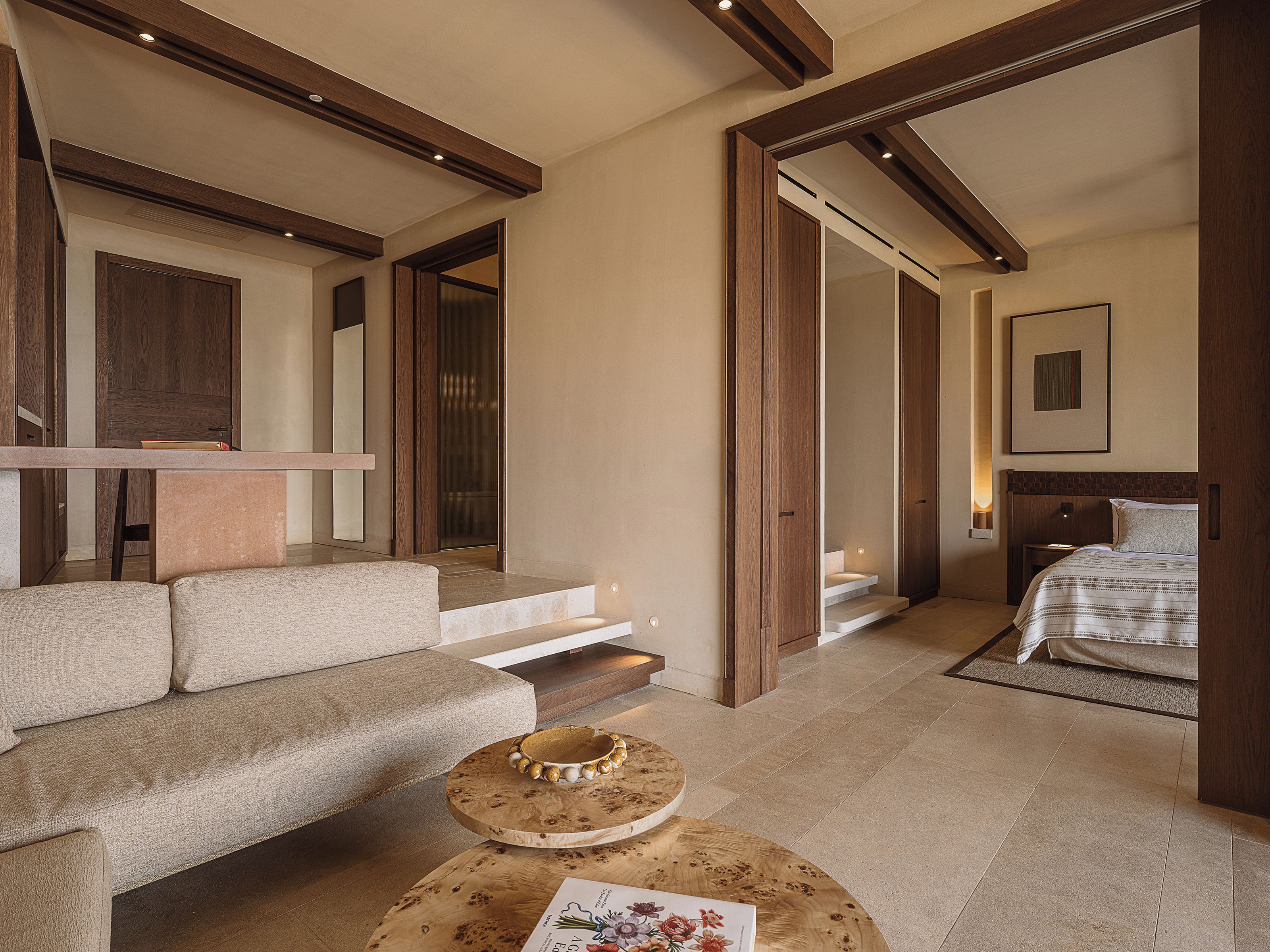A hotel room with a sofa, a wooden coffee table, a bed, and a staircase leading to another room.