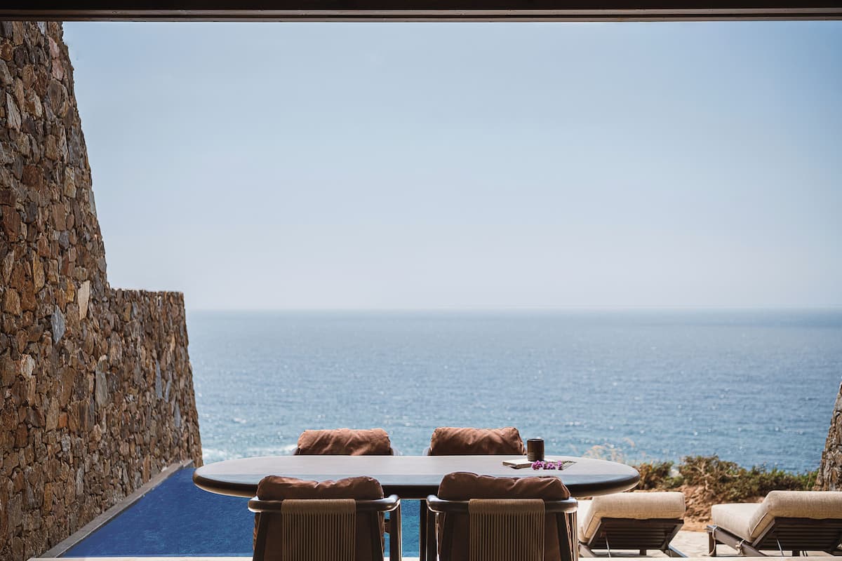A stone wall, a round table with four chairs, and a view of the ocean.