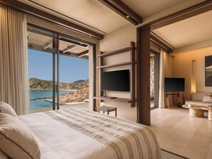 A hotel room with a bed, a TV, a sofa, and a view of the sea.