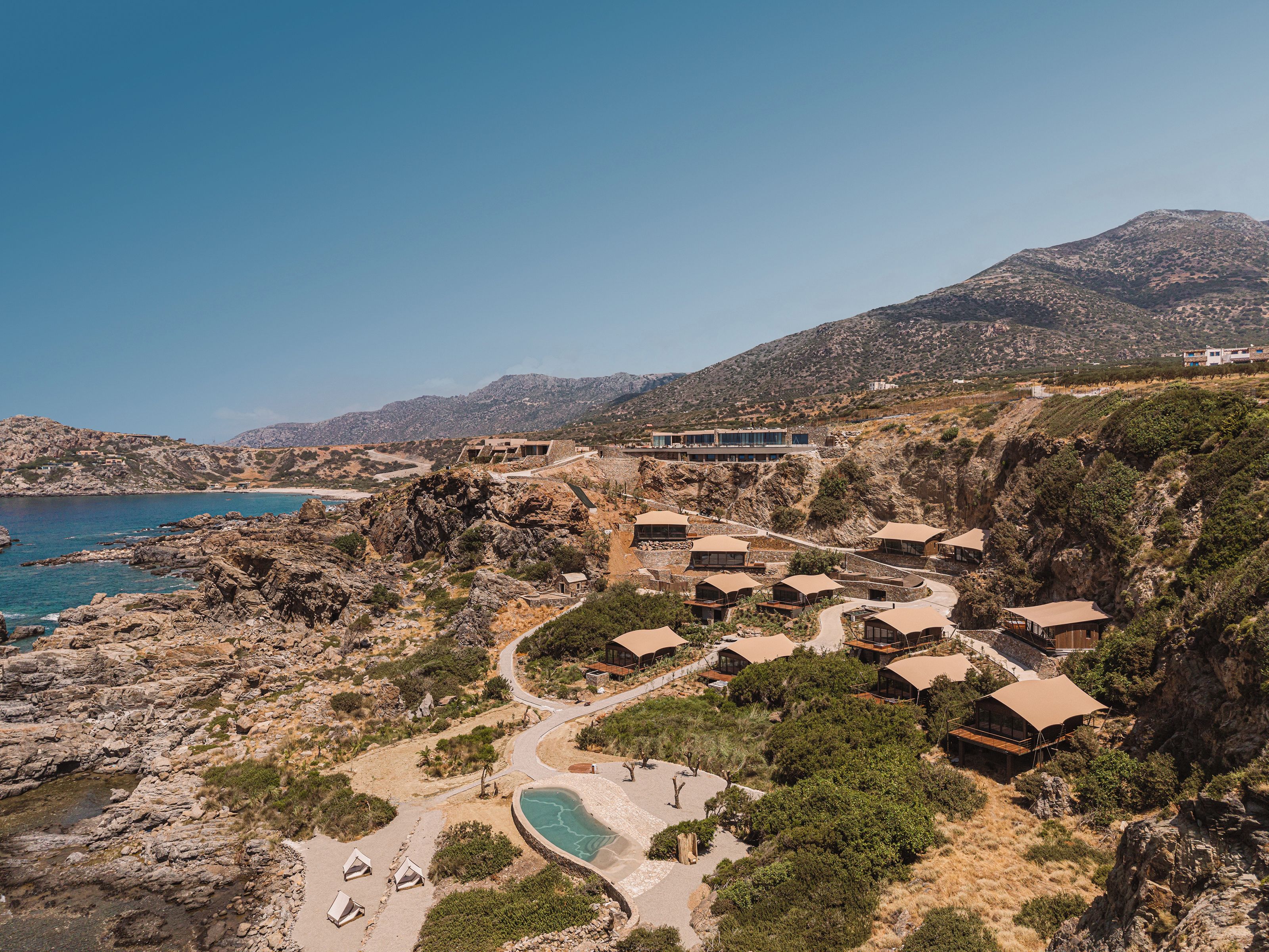 Ein Küstenresort mit mehreren bungalowsartigen Unterkünften, einem Swimmingpool und einer kurvenreichen Straße zum Strand.