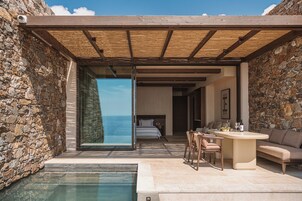 A modern outdoor pool area with a stone wall, a wooden pergola, and a view of the sea.