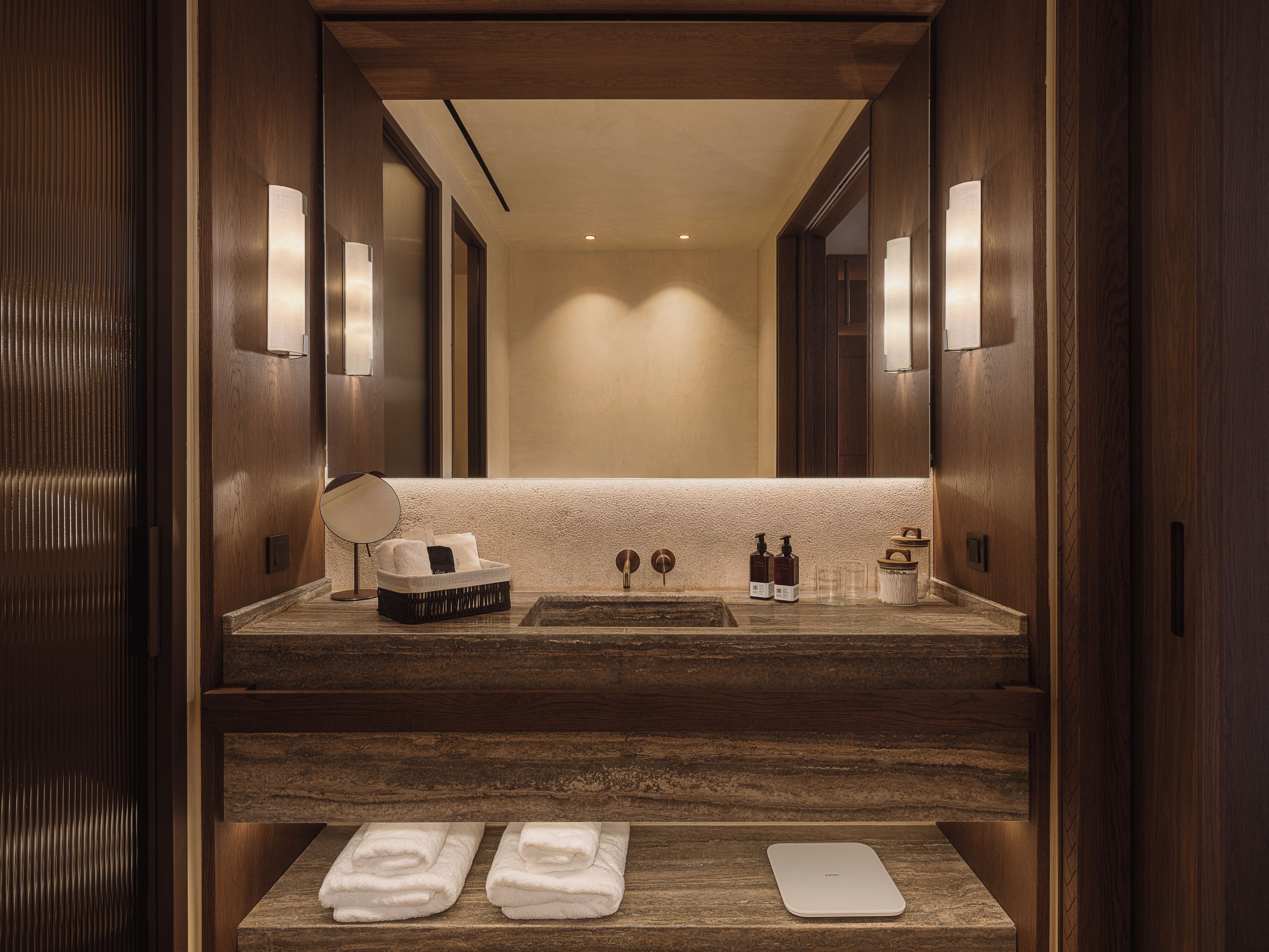 A hotel bathroom with a wooden vanity, a large mirror, two sinks, and a towel rack.