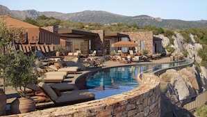 A pool area with lounge chairs and a stone wall. - The Revery, Elafonisi - Member of Leading Hotels of the World (Kissamos)