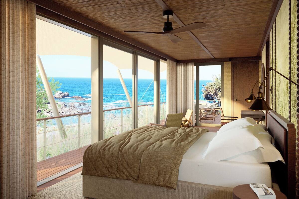 A bedroom with a large bed, a ceiling fan, and a view of the sea.