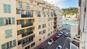 A multi-story building with balconies, a marina with boats, and a hilly landscape in the background.